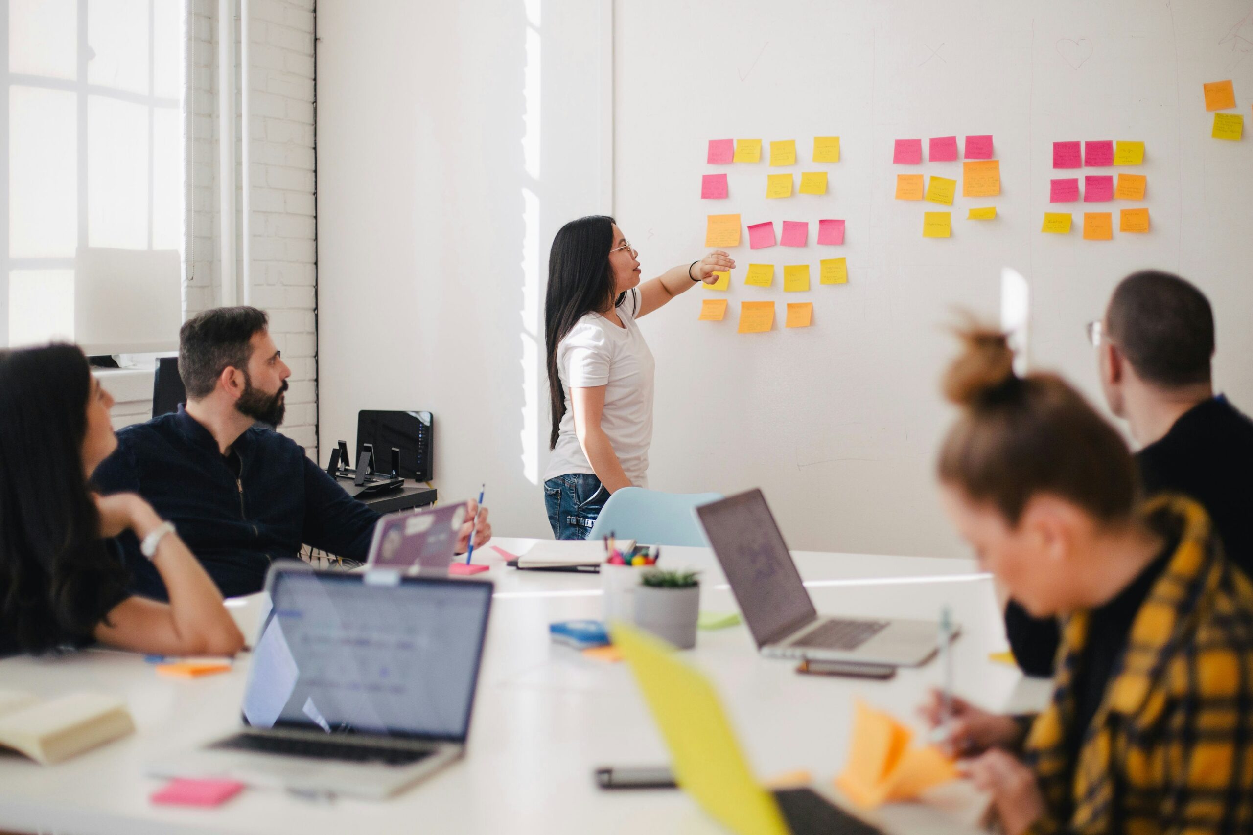 Team members engaged in discussion at an office, with vibrant sticky notes displayed on the wall behind them.