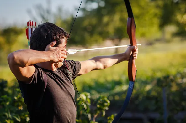 A man focuses intently as he aims a bow and arrow, preparing for a precise shot in a serene outdoor setting.